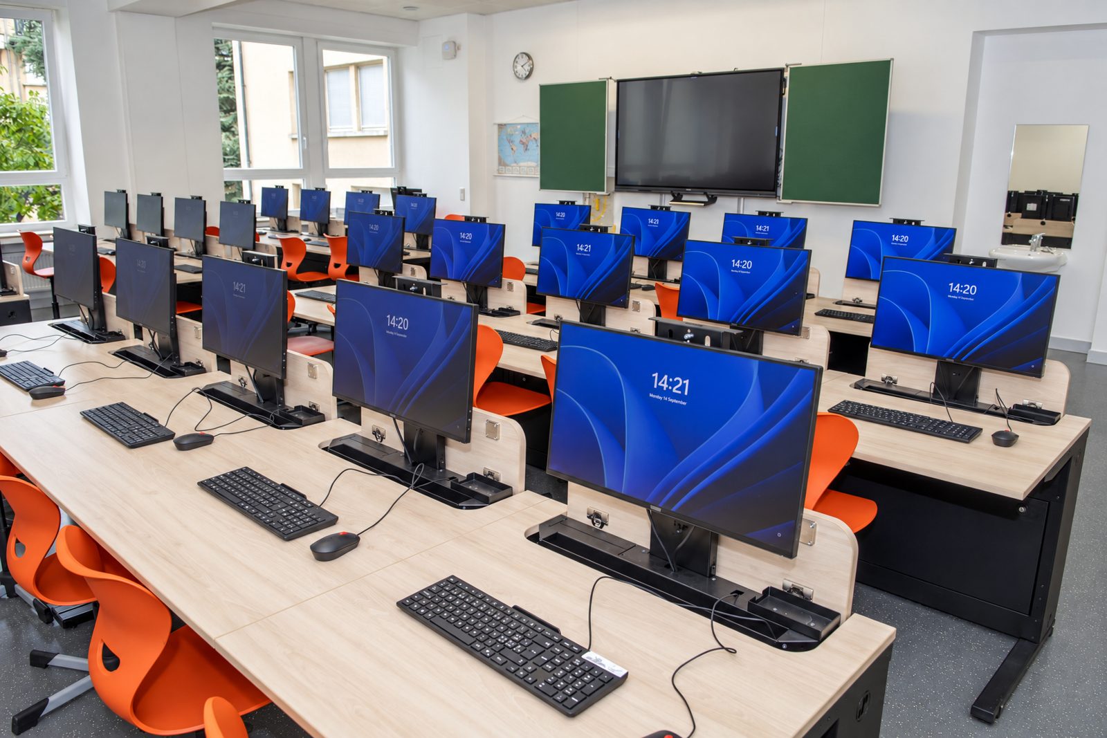 Computerraum der Ecole Privée Fieldgen mit Tischreihen, ausgefahrenen Monitoren, Tafel und Display
