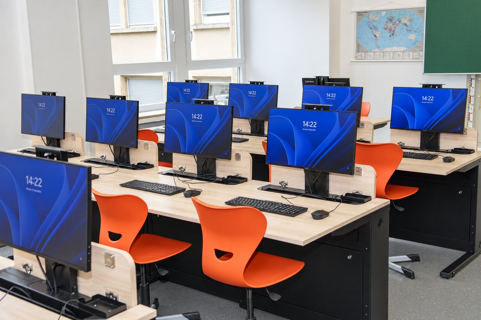 Computerraum der Ecole Privée Fieldgen mit Tischreihen, ausgefahrenen Monitoren und Fensterfront
